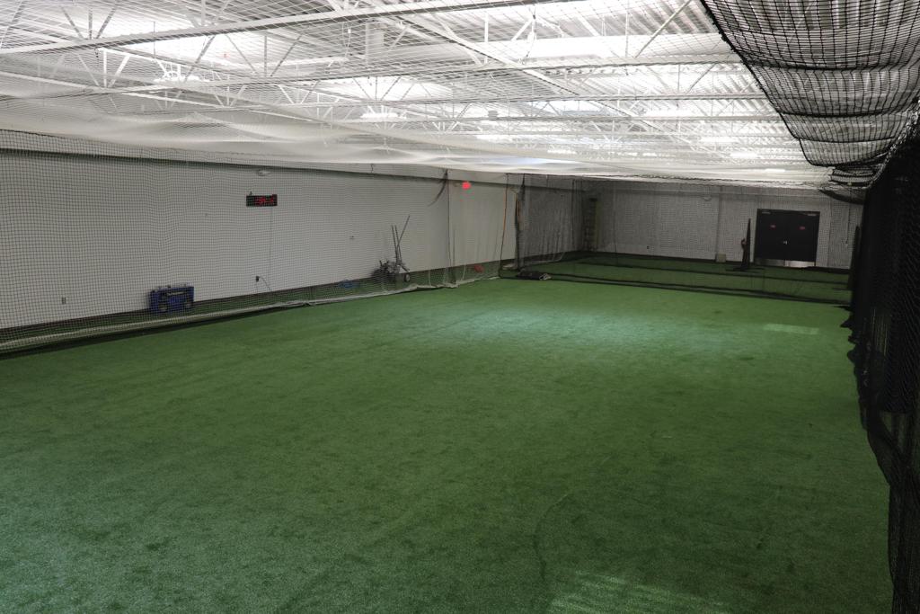 Indoor batting cage with green turf and a ball on a tee